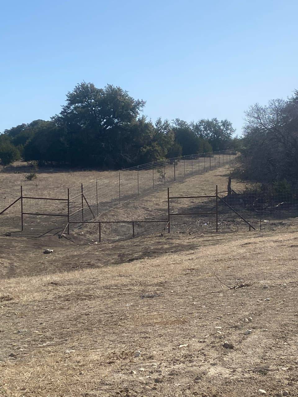 Pipe ranch gate along a rugged, tree-lined trail on a Central Texas property near Hico, TX, built by Linn's Fencing.