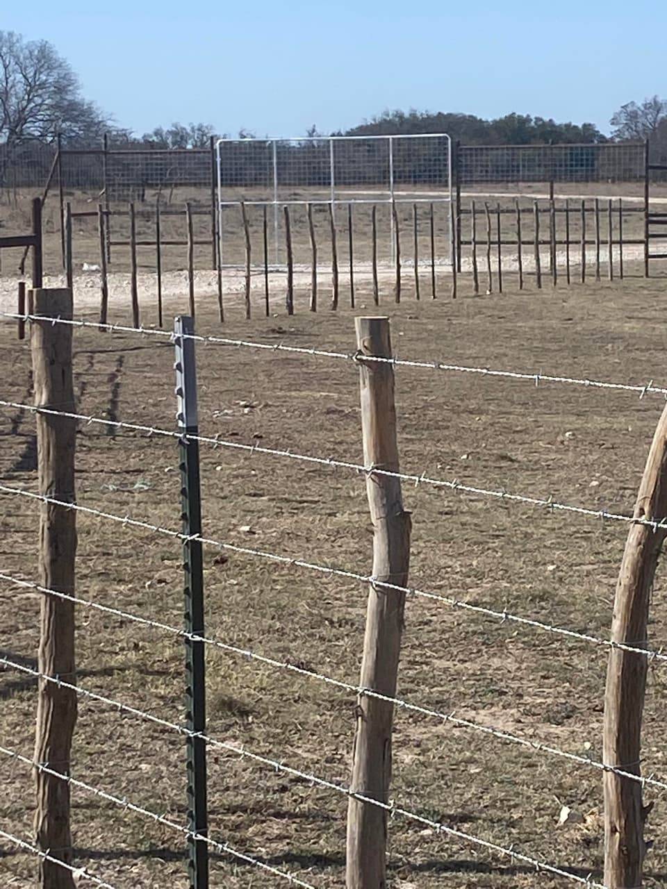 Ranch & Farm Fencing example — Woven field wire fence with wood line posts and corral gate, Central Texas ranch pasture